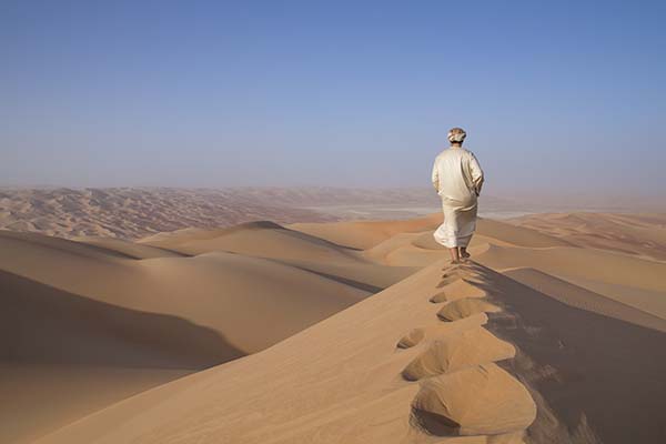 Man in traditional outfit in a desert at sunrise